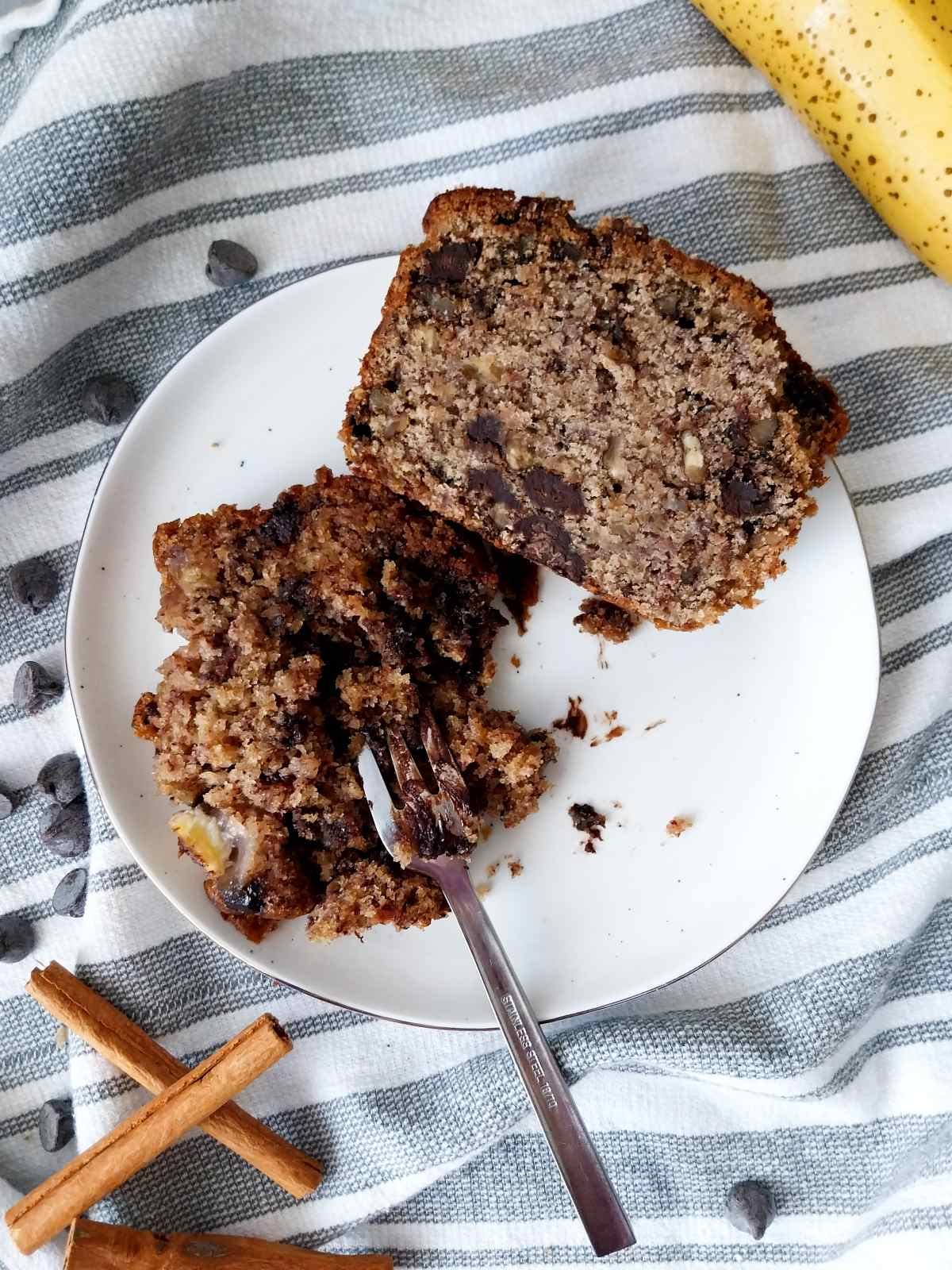 Two banana bread slices on a white plate with a little fork.
