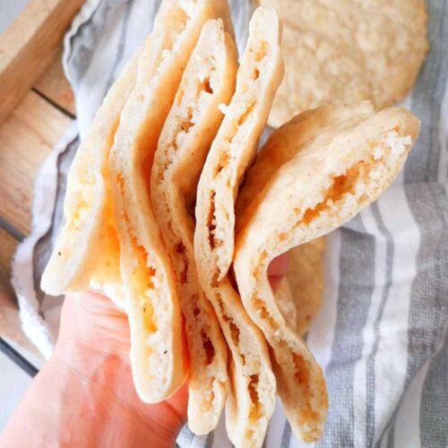 Four gluten-free lebanese pita pocket breads held in a hand up close.