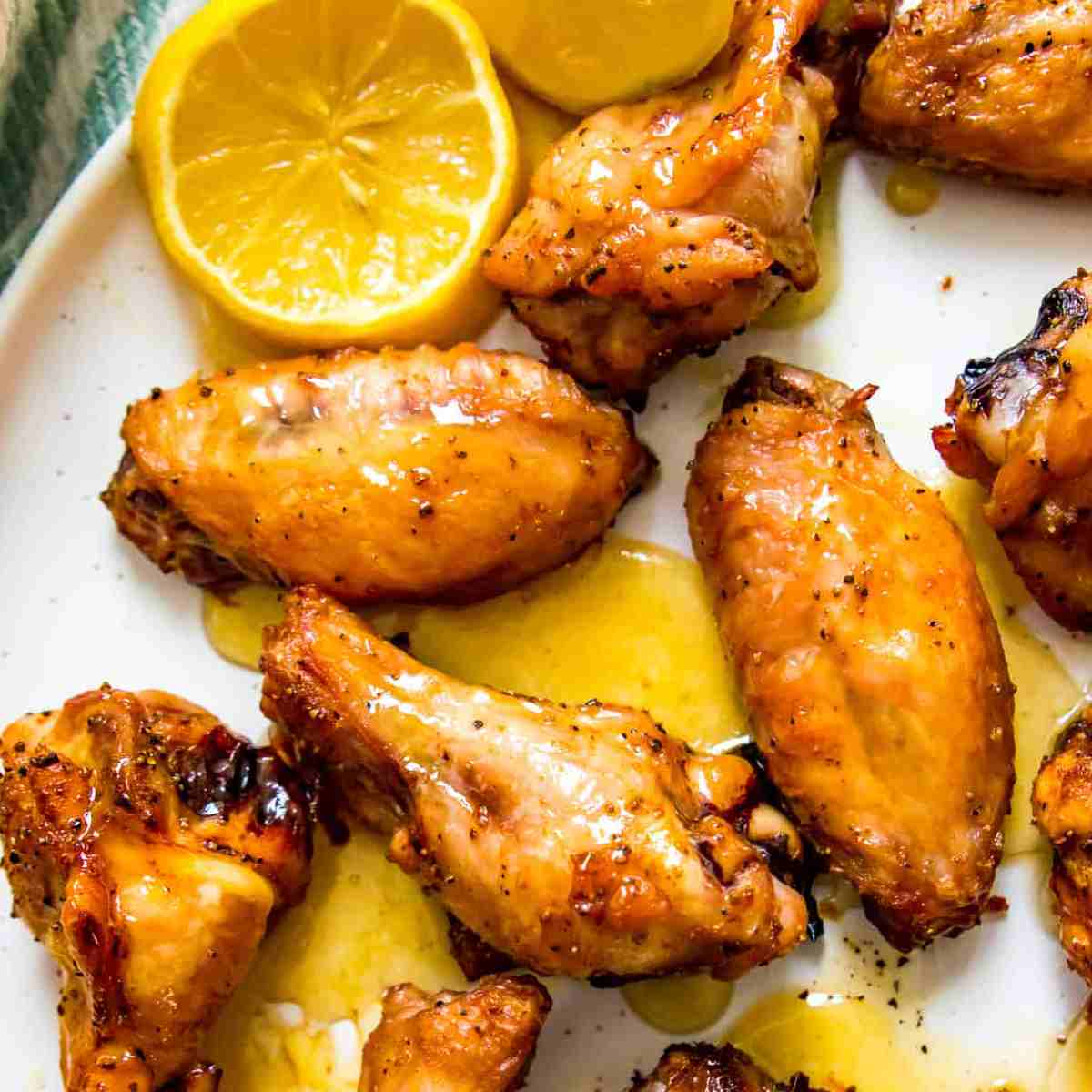 Chicken wings covered in yellow sauce with lemon slices on the side, all on a white plate.