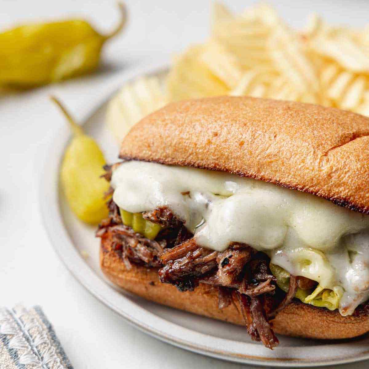 Italian shredded beef sandwich on a white plate with chips in the back.