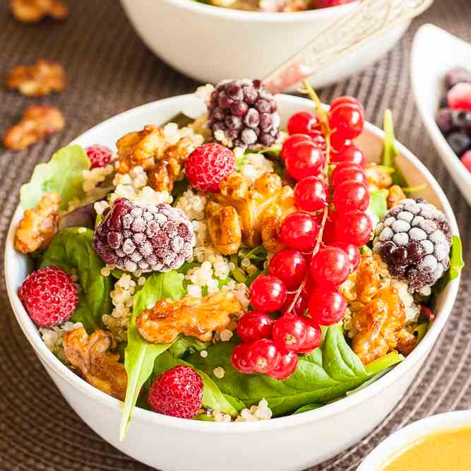 A white bowl with the salad with tons of berries and nuts on top.