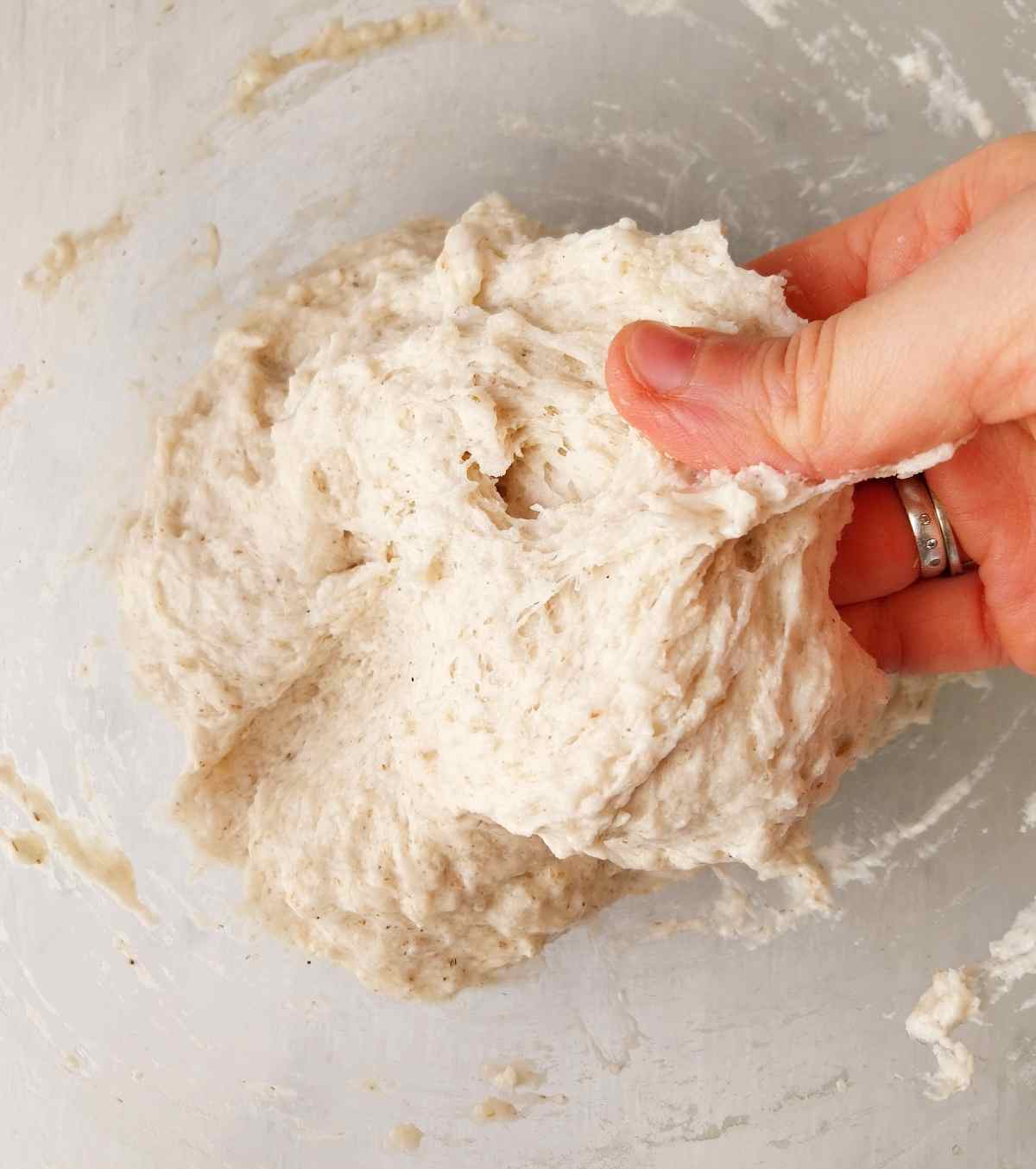 Stretchy dough in a large mixing bowl with a hand pulling it to the side.