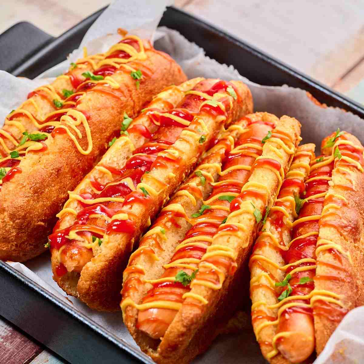 Coconut and almond flour hot dog buns with hot dogs in them  and sauce on the top in a baking dish.