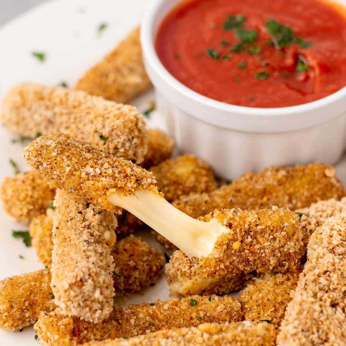 Mozzarella sticks on a white plate with red sauce on the side.