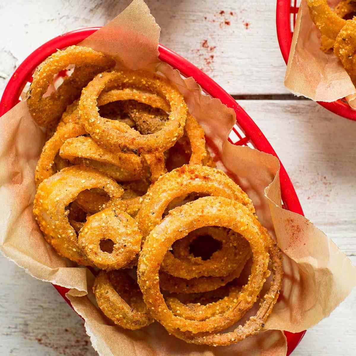 Onion rings in a red basket lined with paper, a sauce on the side.