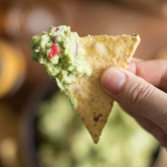 Guacamole on a tortilla chip up close, held by a hand.