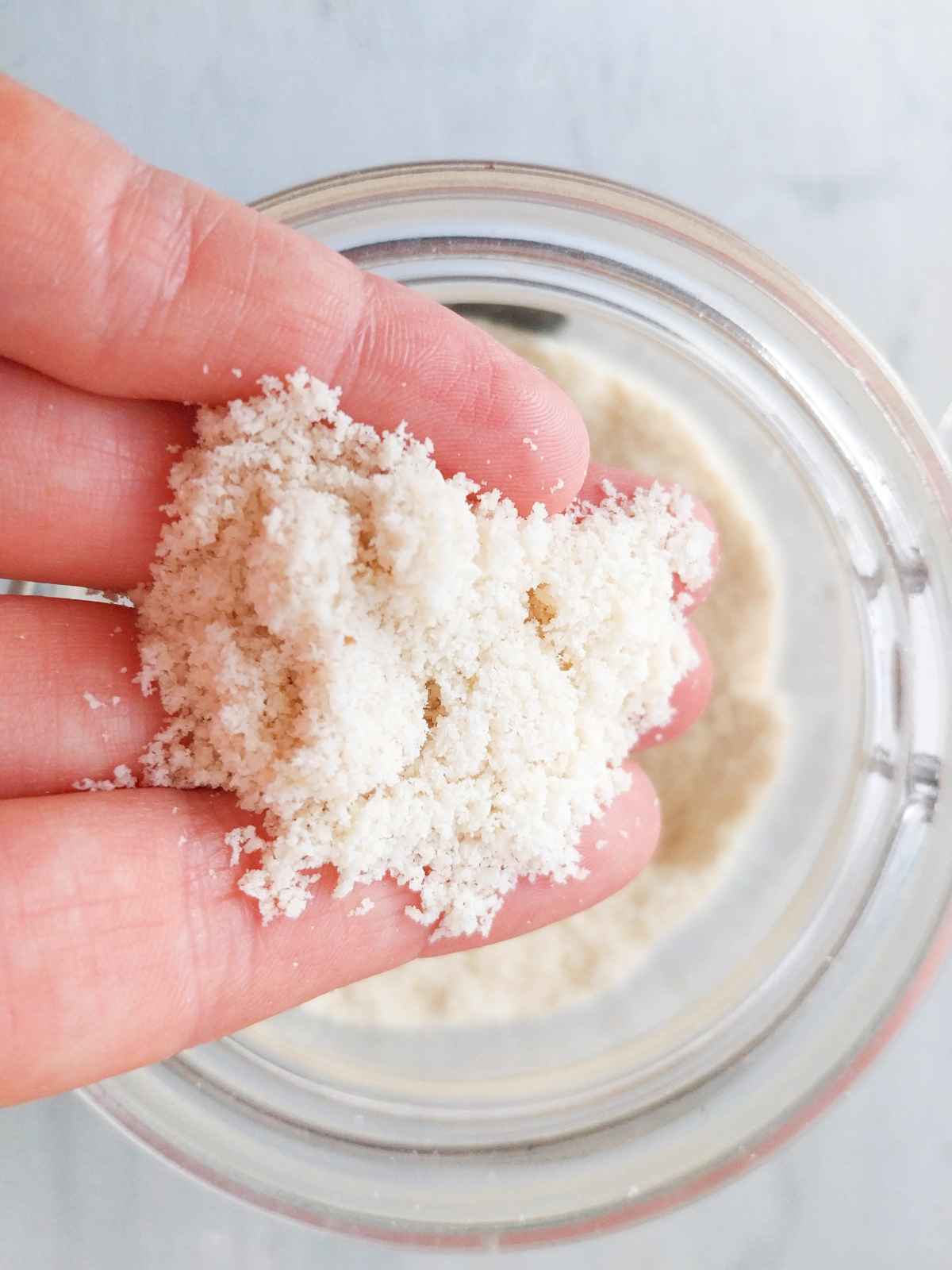 Homemade Almond flour held in a hand over a glass jar.