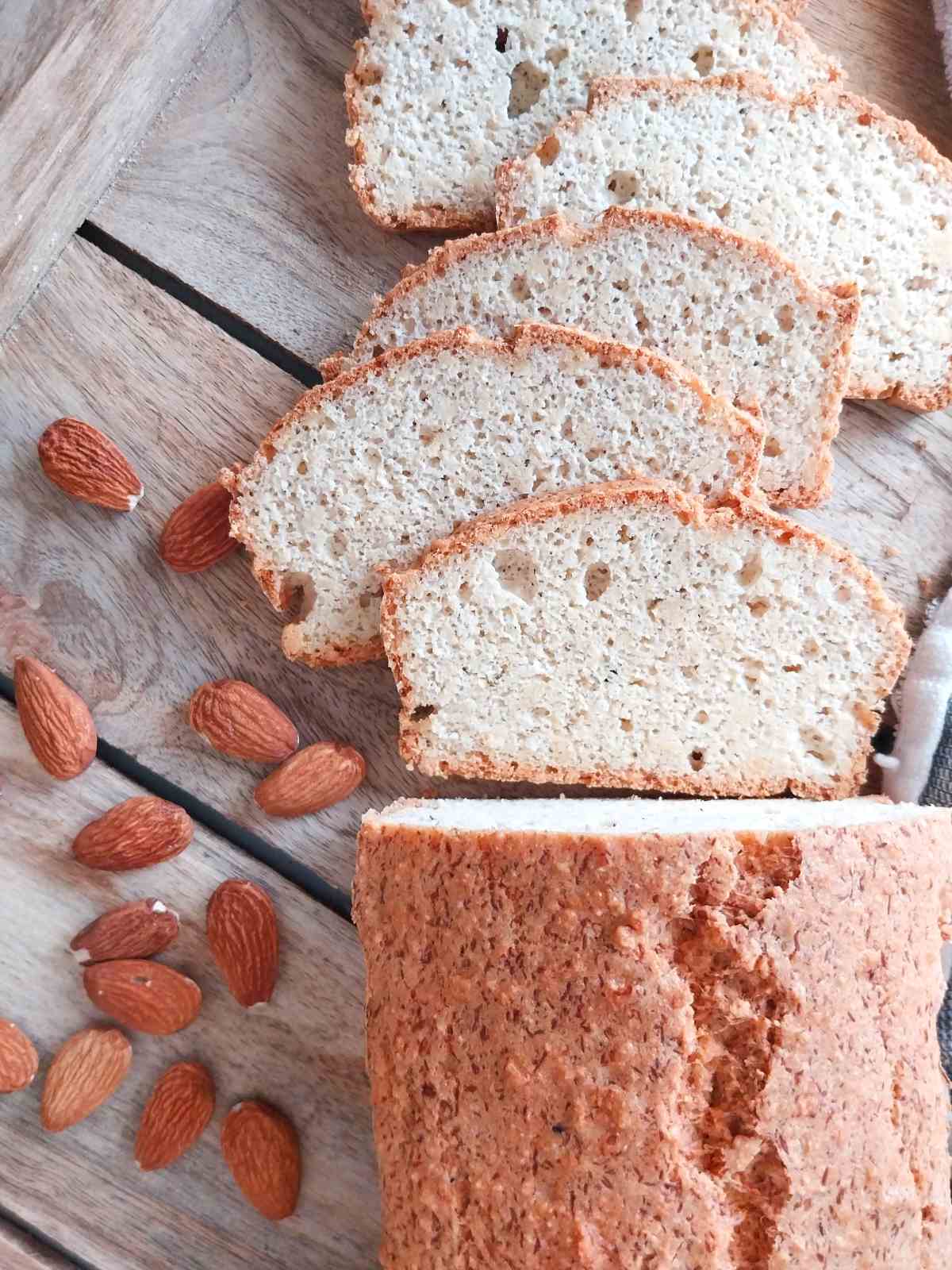 Low carb almond bread sliced with almonds next to it on a wooden surface.