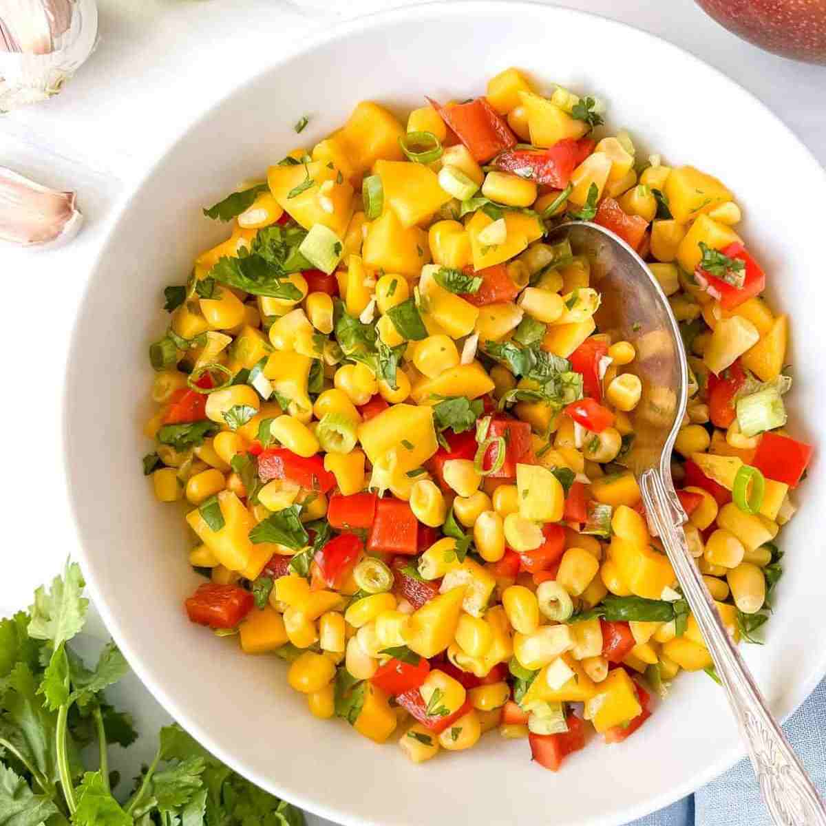 Mango and corn salsa in a white bowl with a spoon in it.
