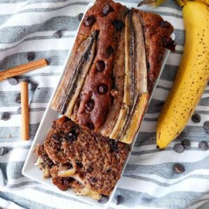 Banana bread sliced on a white plate with a banana on the side.