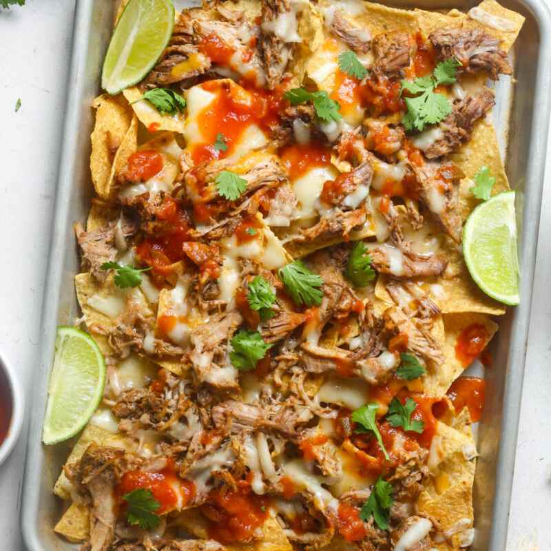 A tray with pulled pork nachos and lime slices on the sides of the tray.
