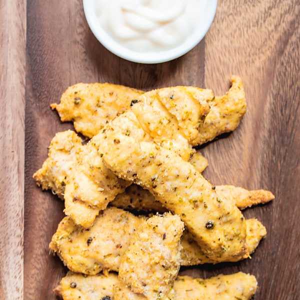 Parmesan chicken tenders with a side sauce on a wooden board.