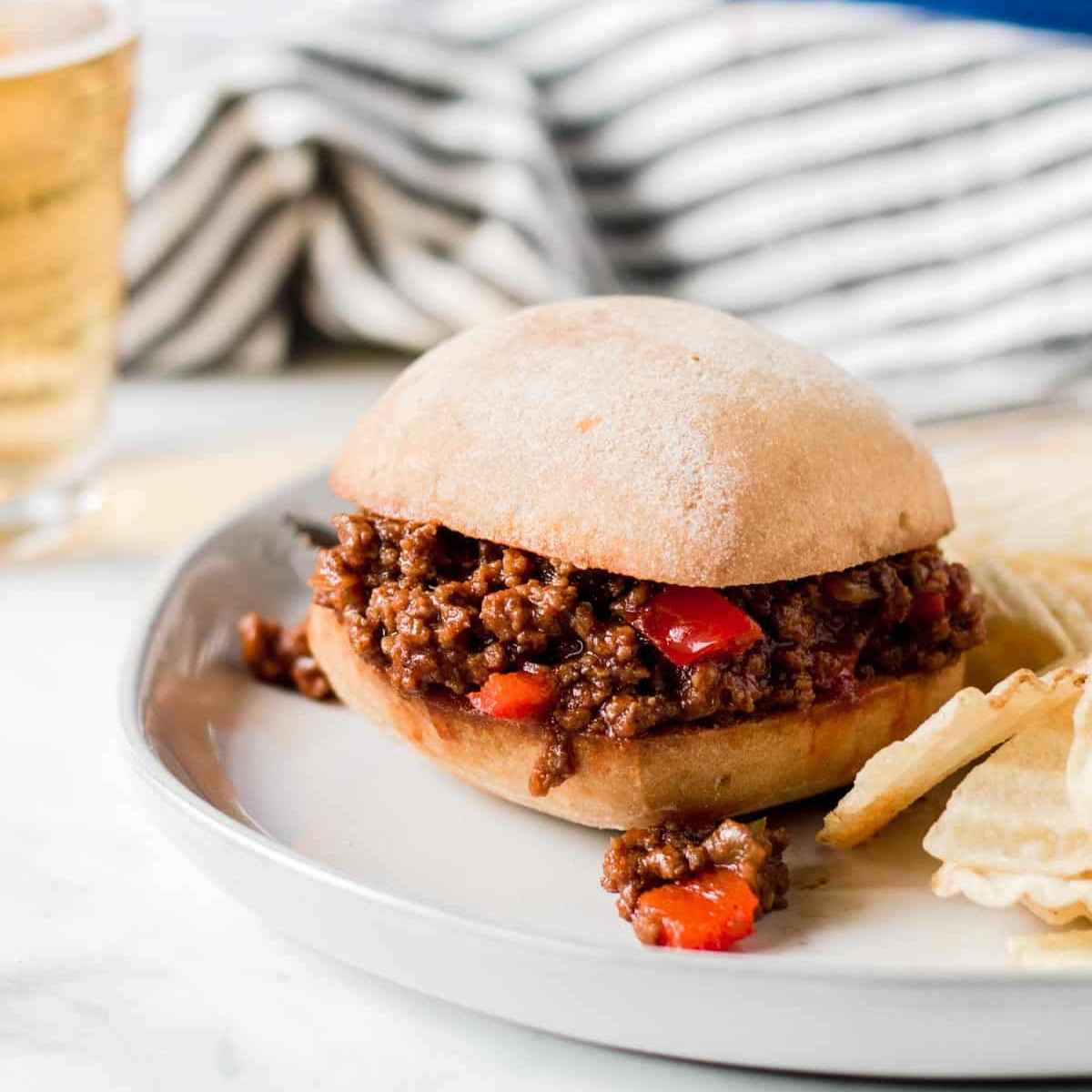 Gluten-free sloppy joe sandwich on a large white plate with chips on the side.