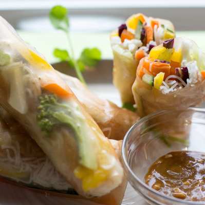 A few spring rolls placed on a white plate with a dipping sauce on the side.