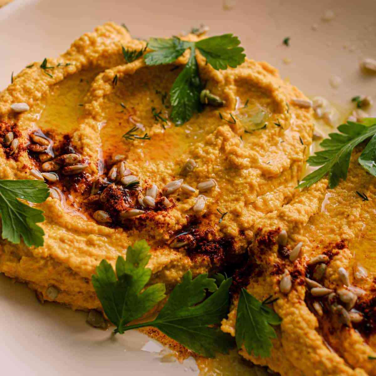 Sunflower dip with sunflower seeds and cilantro on top on a white surface.