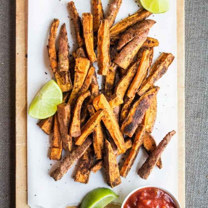 sweet potato fries on a whtie board with slices of lime on the side. 