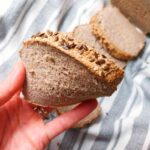 A slice of buckwheat bread in a hand with more slices in the background on a kitchen towel.