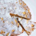 Buckwheat apple cake with a slice cut out on a white surface.
