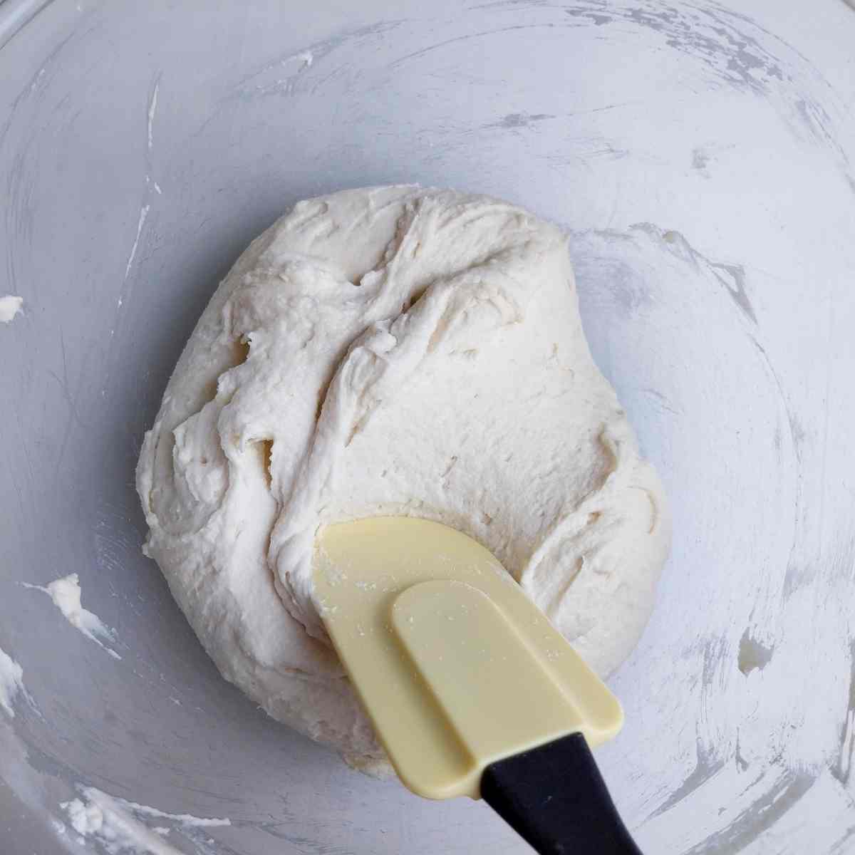 Mixed dough in a glass bowl with a rubber spatula.
