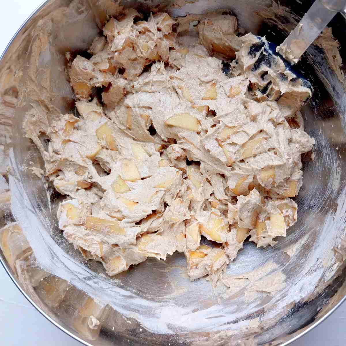 Mixing apple sliced into the batter with a rubber spatula.