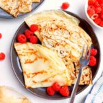 Gluten-free sourdough crepes on a plate with raspberries on the side.
