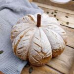 Gluten-free pumpkin sourdough baked and decorated with a cinnamon stick on a wooden surface.