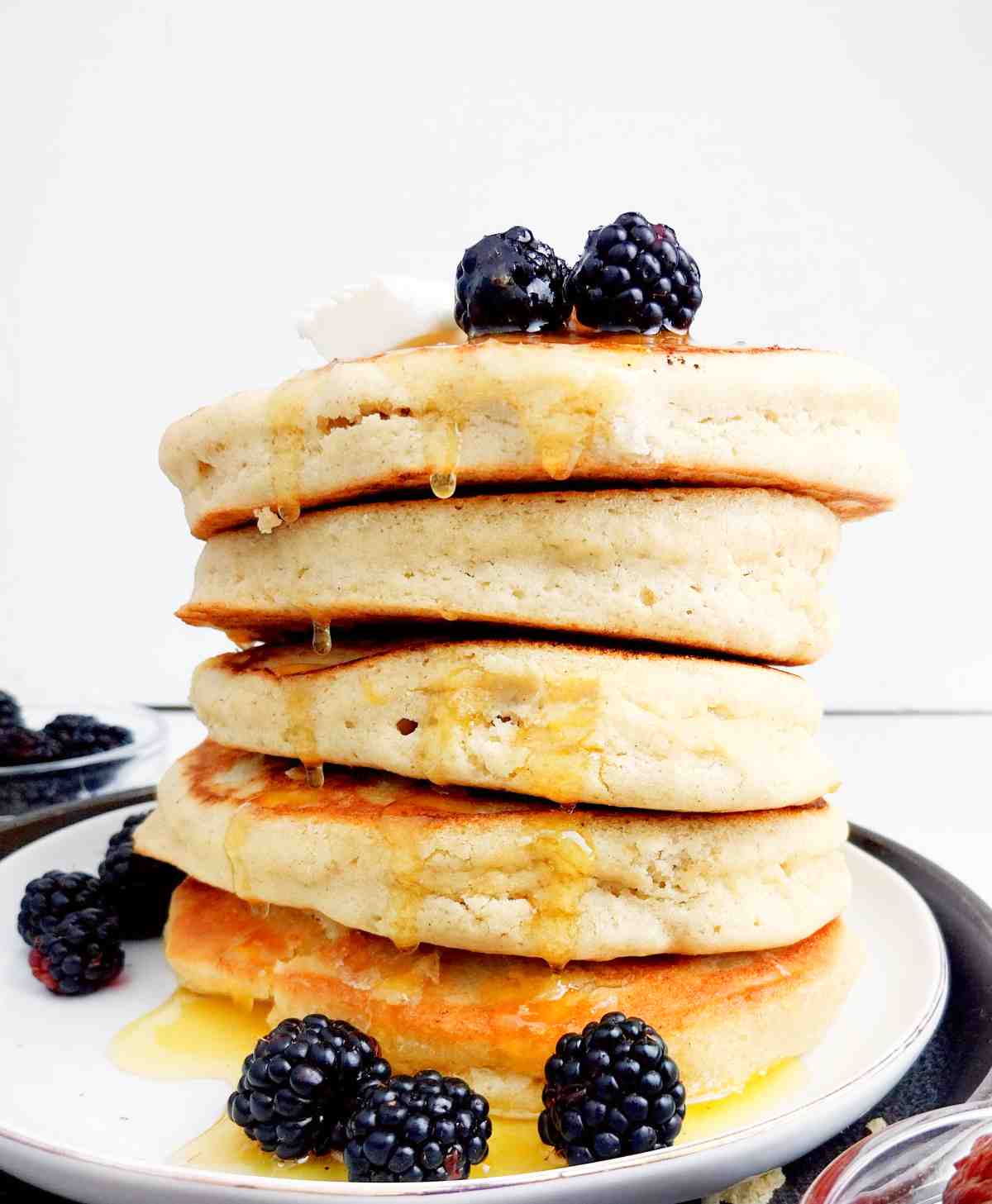A stack of buckwheat pancakes with blackberries and honey dripping from the top.