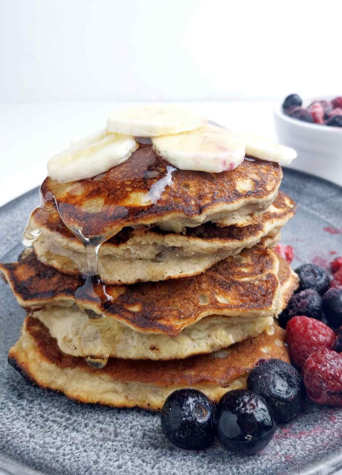 A stack of banana pancakes with banana slices on top and berries on the side.