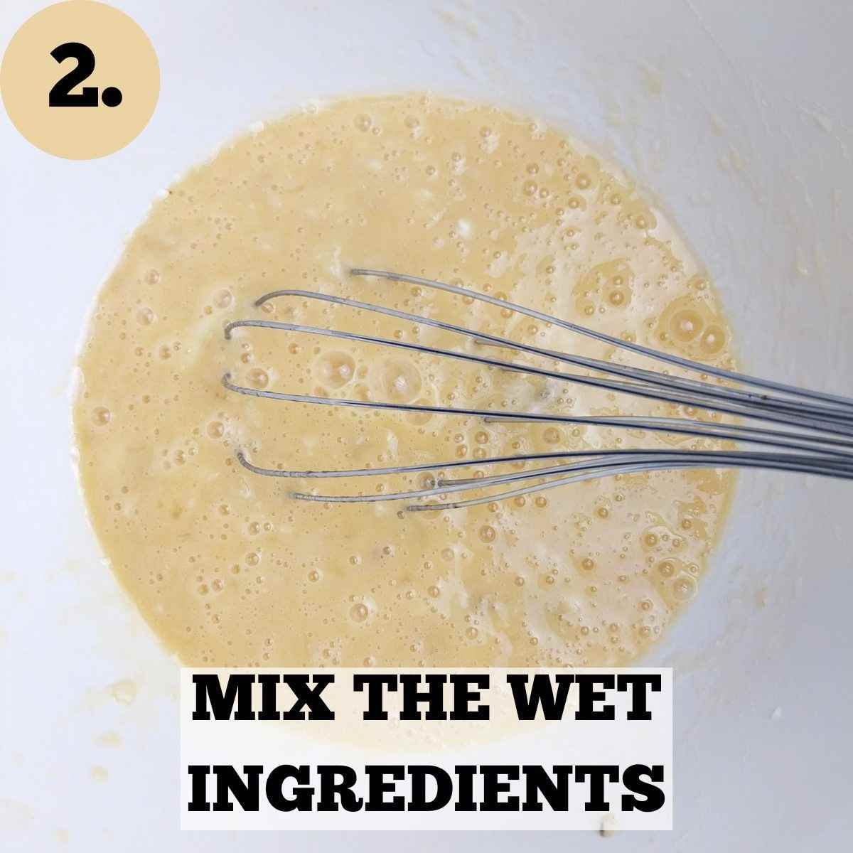 Mashed bananas mixed with the wet ingredients in a white bowl with a whisk.