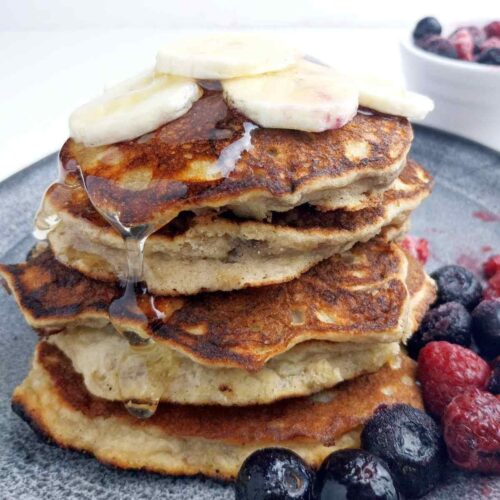 A stack of banana pancakes with banana slices on top and berries on the side.