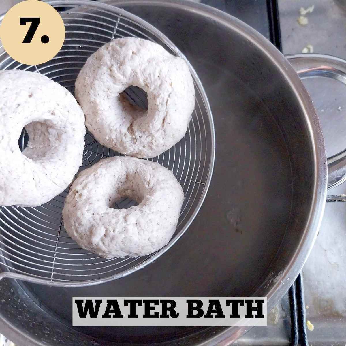 Three raw bagels on a spider spoon over a pot with boiling water.