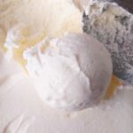 A scoop of white ice cream with the ice cream scooper next to it.