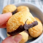 Rocher coco cookie held in a hand by two fingers with the rest of the Rocher cocos in the background in a bowl.