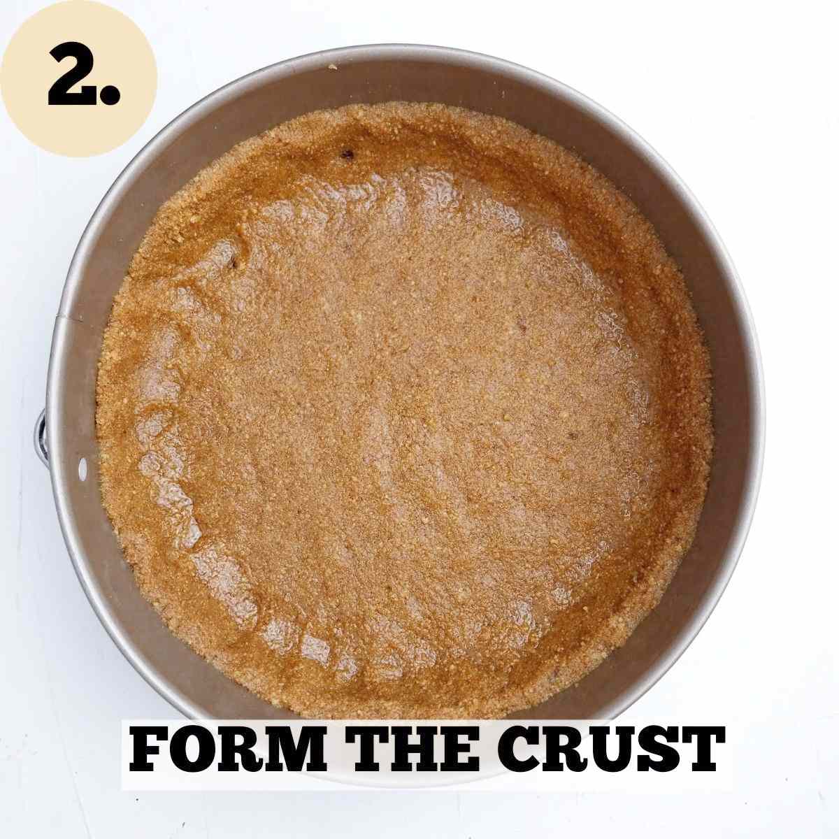 A round cake pan with formed graham cracker crust inside of it on a white surface.