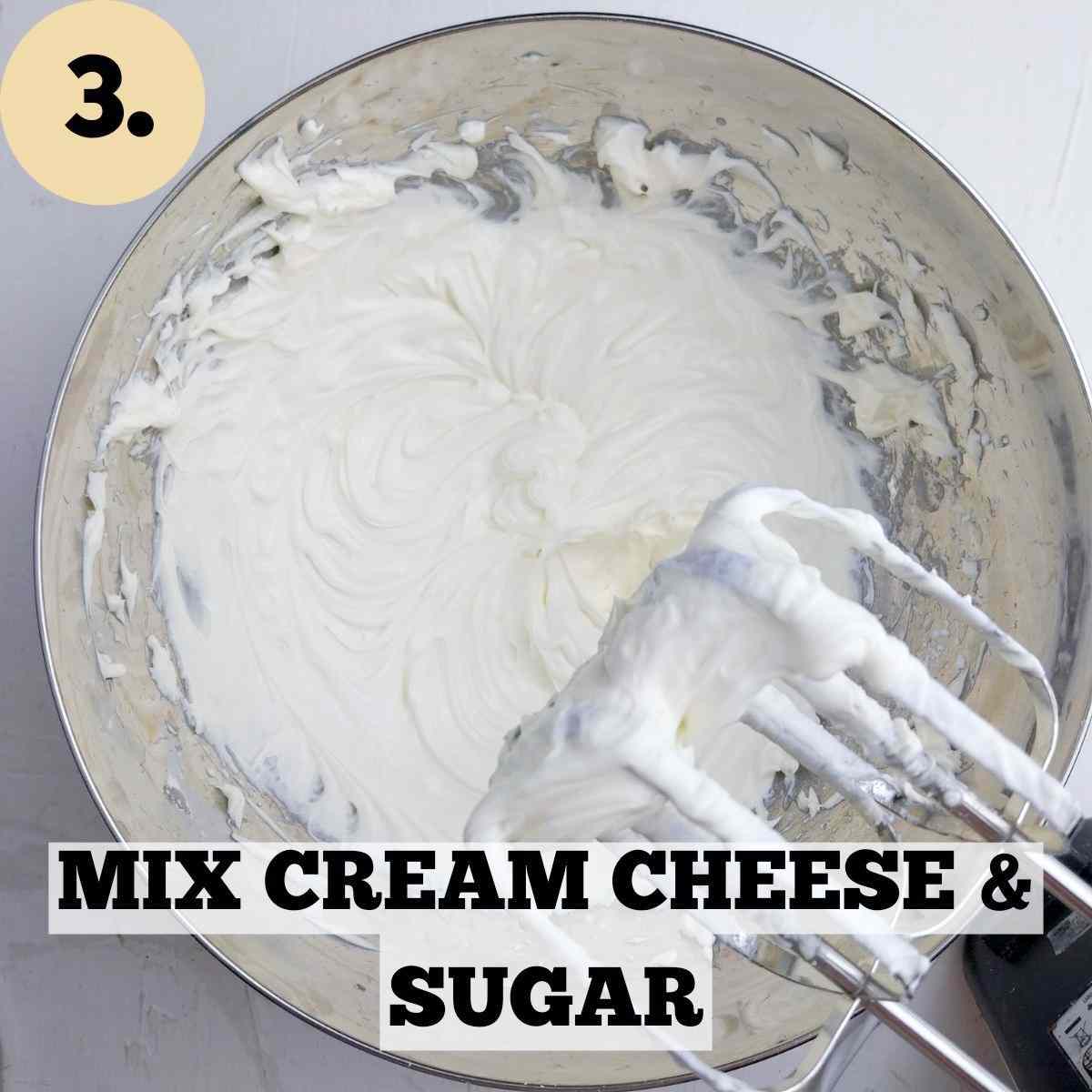 White mixture of cream cheese and powdered sugar in a metal bowl with electric beaters on the side.