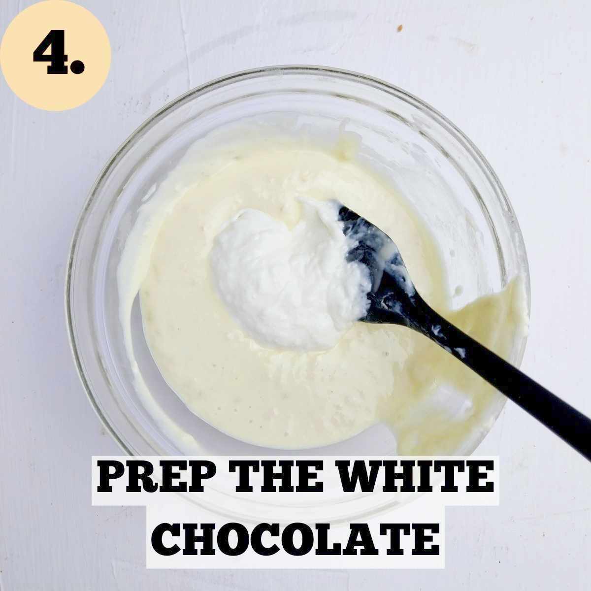 A glass bowl with melted white chocolate and a spoon of cream cheese in it with a black rubber spatula dipped in the mixture.