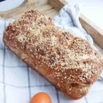 A gluten free tsoureki loaf on a kitchen towel against a wooden surface.