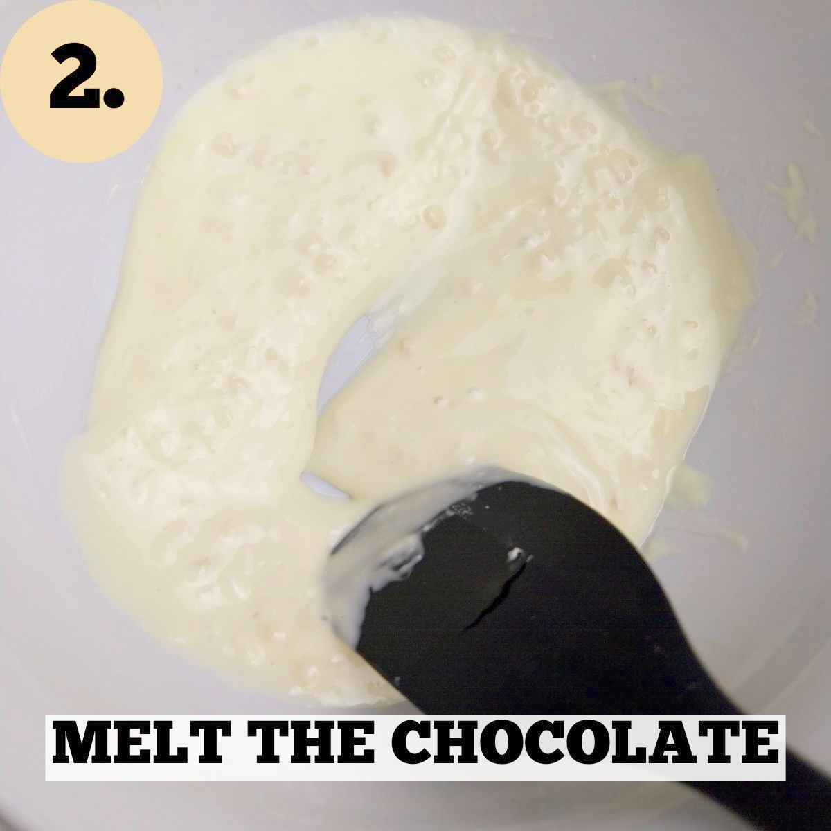 Melted white chocolate in a white mixing bowl with a black silicone spatula.