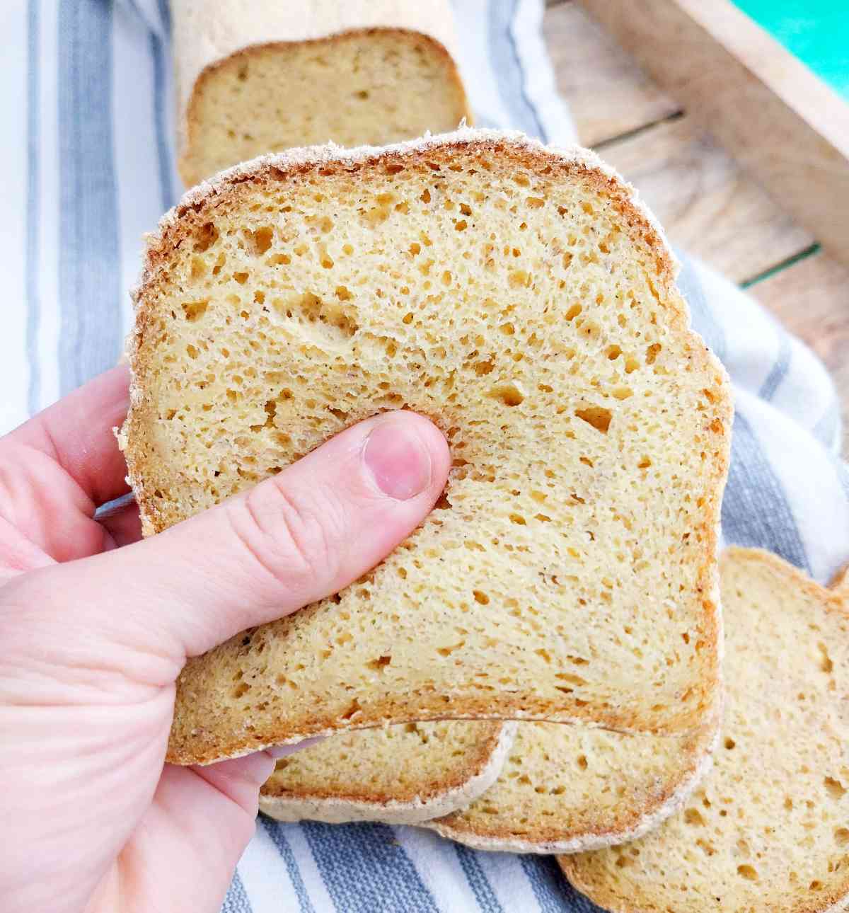 A slice of corn flour bread up close with the rest of the loaf in the background on a kitchen towel.