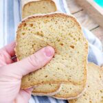 A slice of corn flour bread up close with the rest of the loaf in the background on a kitchen towel.
