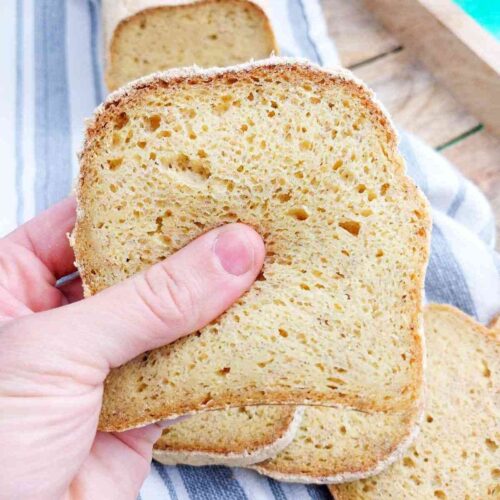A slice of corn flour bread up close with the rest of the loaf in the background on a kitchen towel.