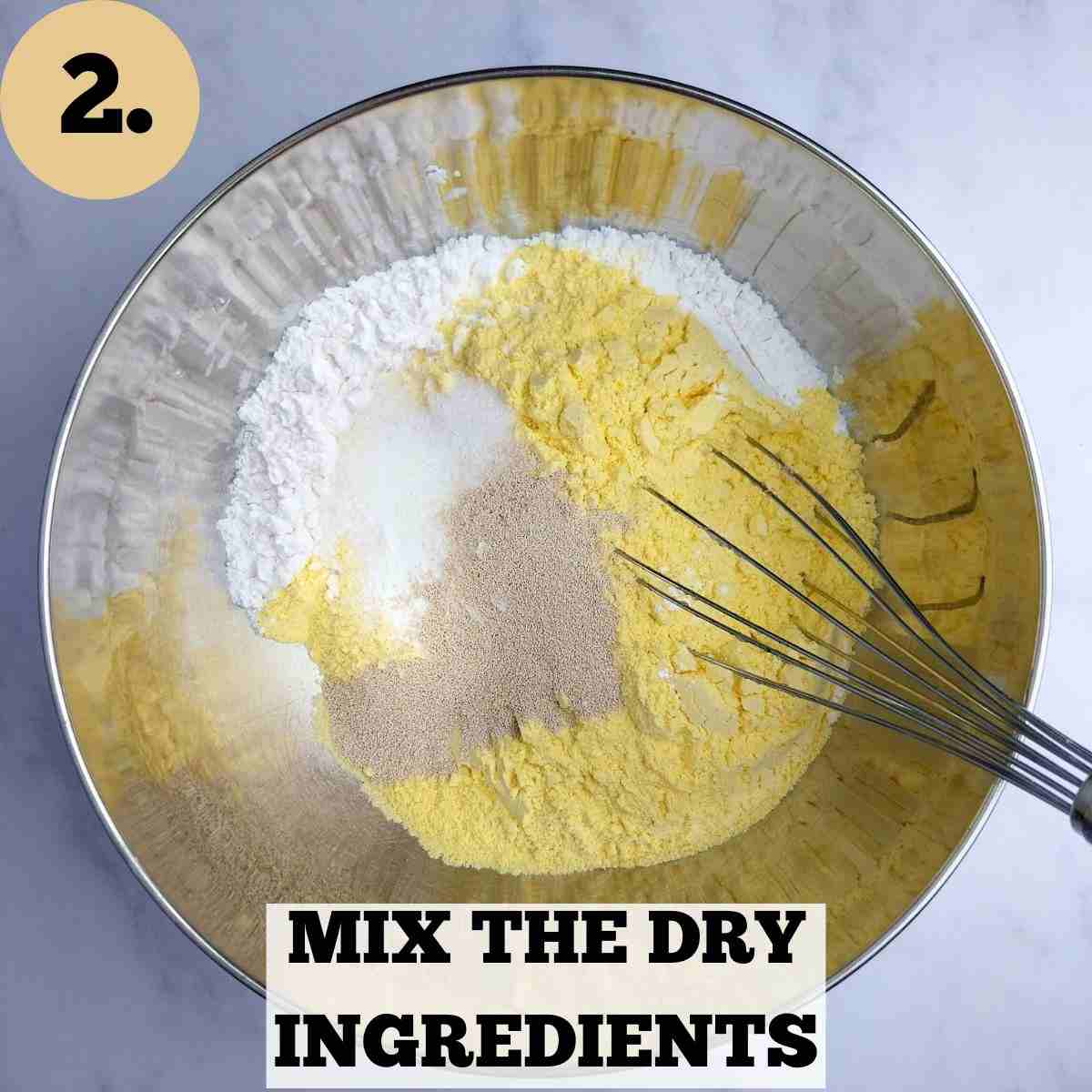 Dry ingredients for corn flour bread in a metal bowl with a whisk in it.