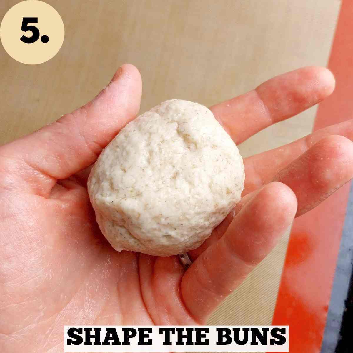 A small dough ball in a hand with a silicone baking mat in the background.