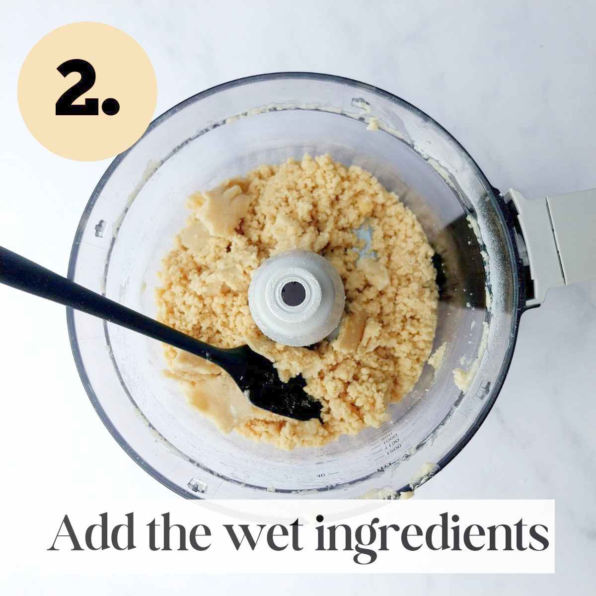 Blended dough in a food processor with a black spatula in it against a white background.