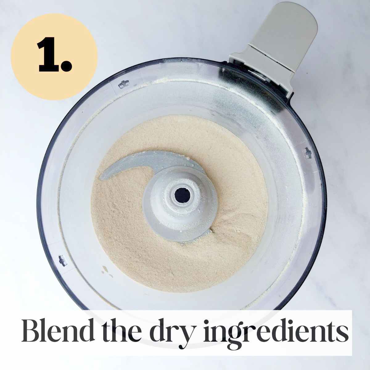 Dry ingredients in a food processor with a blade in it on a white background.
