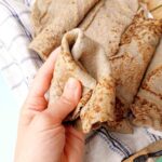 Bajra roti bent in a hand with the rest rotis in the background.