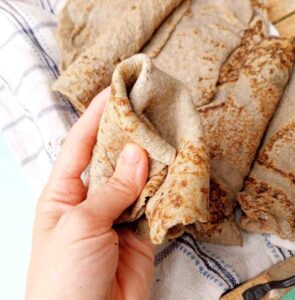 Bajra roti bent in a hand with the rest rotis in the background.
