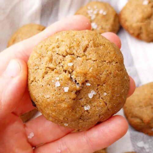 Finger millet cookie in a hand with the rest of the cookies in the background on a kitchen towel.