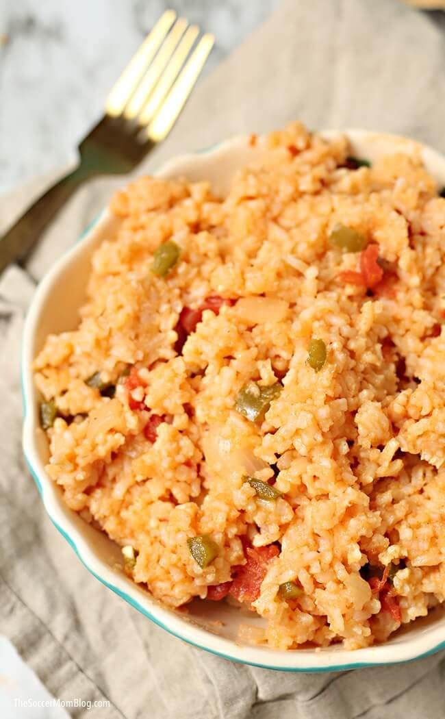 A bowl of golden mexican rice in with a fork in the background.