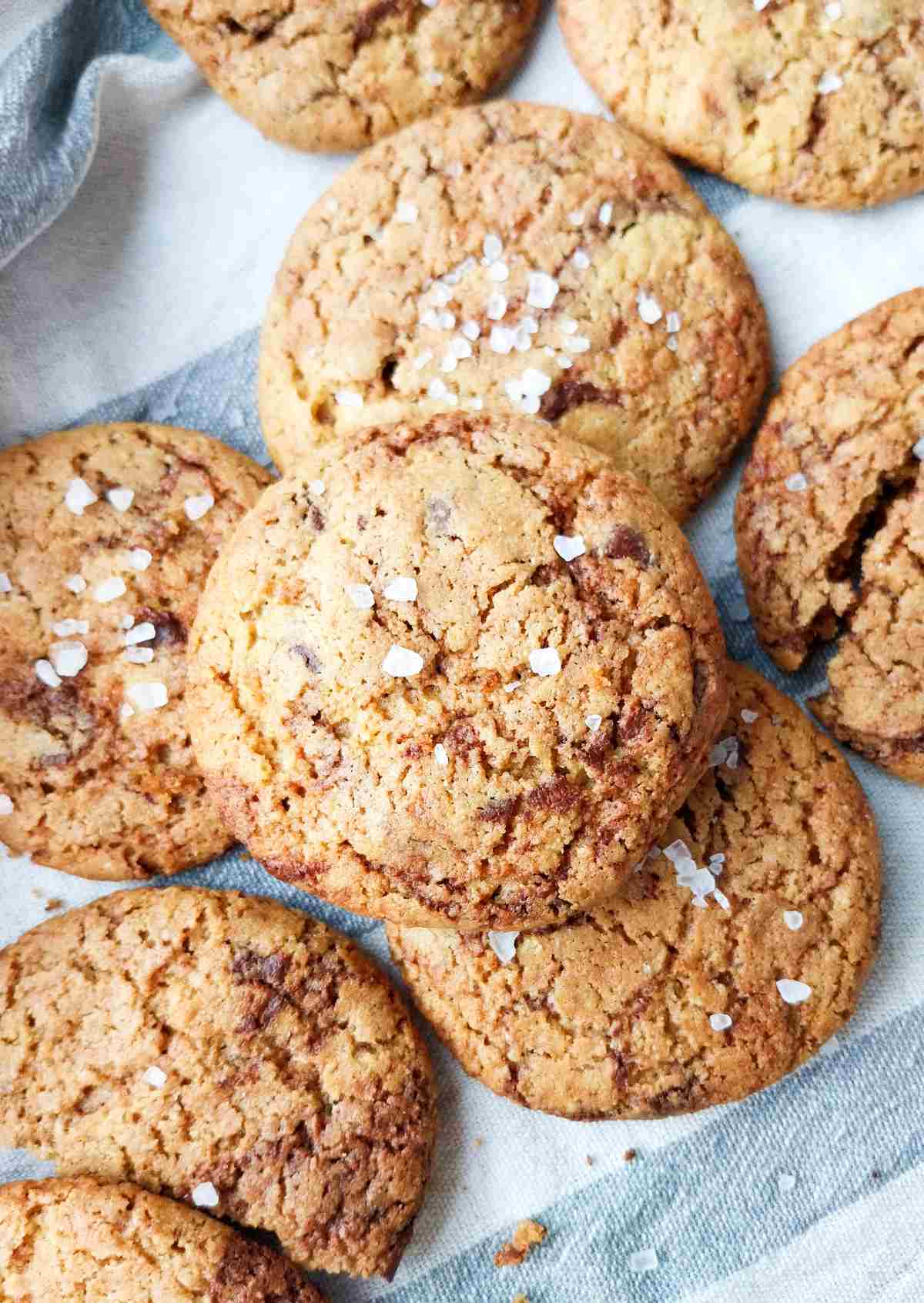 Millet cookies with flaky salt sprinkled on them on a kitchen towel on top of each other.